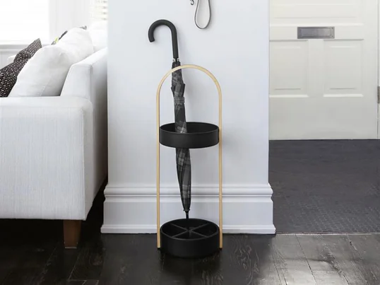 Le porte-parapluies Hub d'Umbra dans la vue d'ambiance : les parapluies à canne peuvent être facilement posés sur le porte-parapluies Hub, tandis que les petits parapluies de poche peuvent être fixés au crochet mural Hub et s'égoutter.