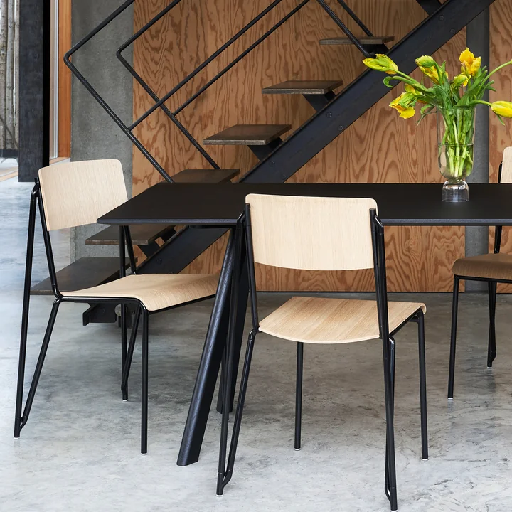 La chaise Petit Standard, noir / chêne laqué mat par HAY sur une table noire à côté de l'escalier