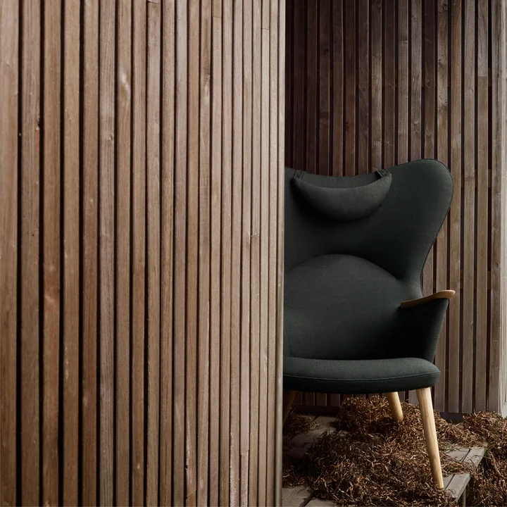 Le site CH78 Mama Bear Lounge Chair de Carl Hansen entre des murs de bois rustiques