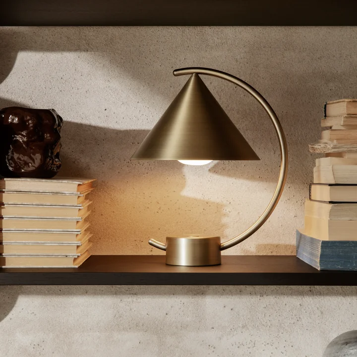 La lampe de table Meridian de Ferm Living en laiton sur une étagère entre des livres