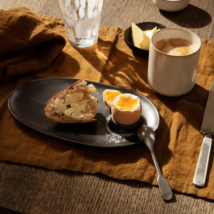 L'assiette de petit-déjeuner Flow de Ferm Living avec du pain et un œuf sur une nappe brune