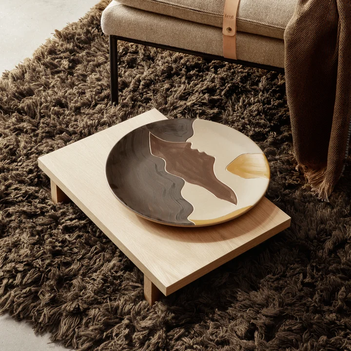 La table d'appoint Kona Low de Ferm Living sur un tapis marron confortable à côté d'un daybed