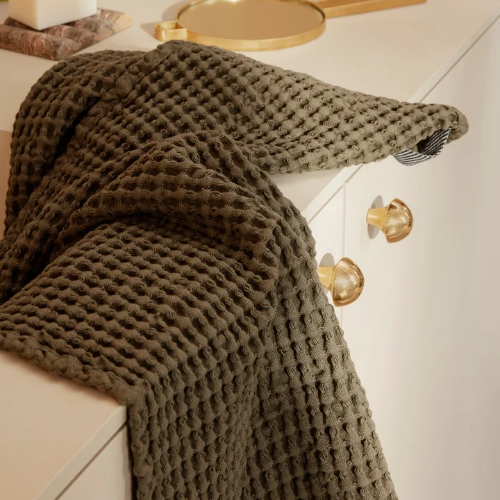 Le drap de bain Organic de Ferm Living en olive sur l'armoire du lavabo dans la salle de bain