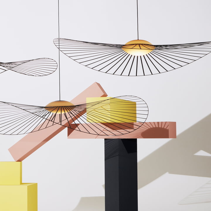 La lampe suspendue Vertigo Nova de Petite Friture à côté d'objets d'art colorés