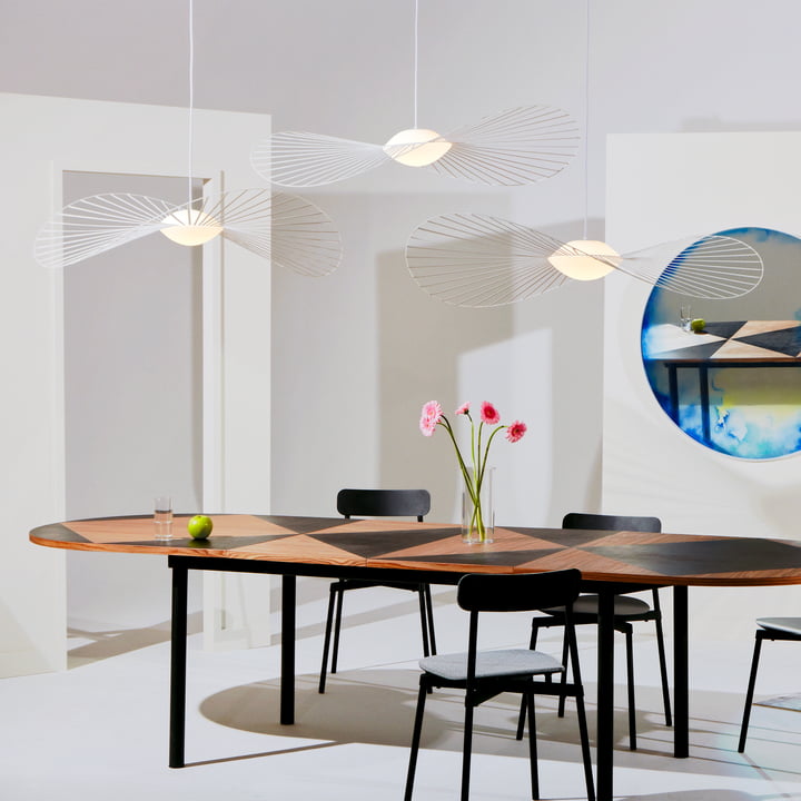 Le luminaire suspendu Vertigo Nova de Petite Friture en groupe au-dessus d'une table de salle à manger ovale en bois avec des chaises noires