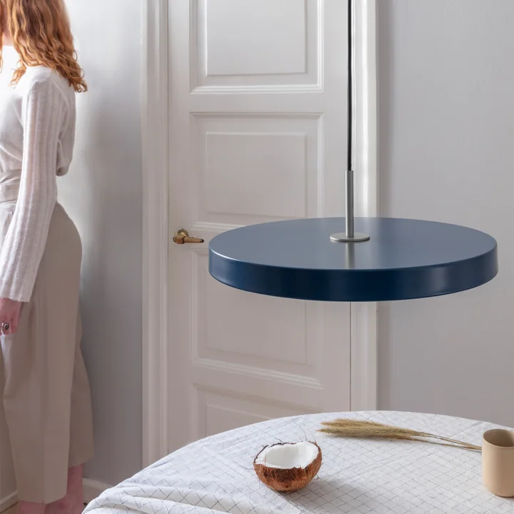 La suspension LED Asteria de Umage en acier / pétrole au-dessus d'une table de salle à manger ronde avec un plafond à carreaux