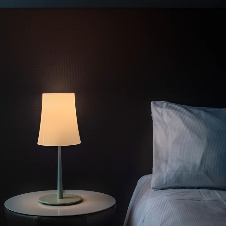 La lampe de table Birdie Easy de Foscarini sur une table de chevet à côté du lit