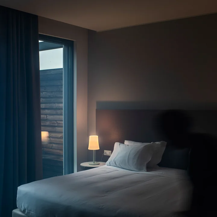 La lampe de table Birdie Easy de Foscarini sur la table de chevet à côté d'un lit près de la fenêtre