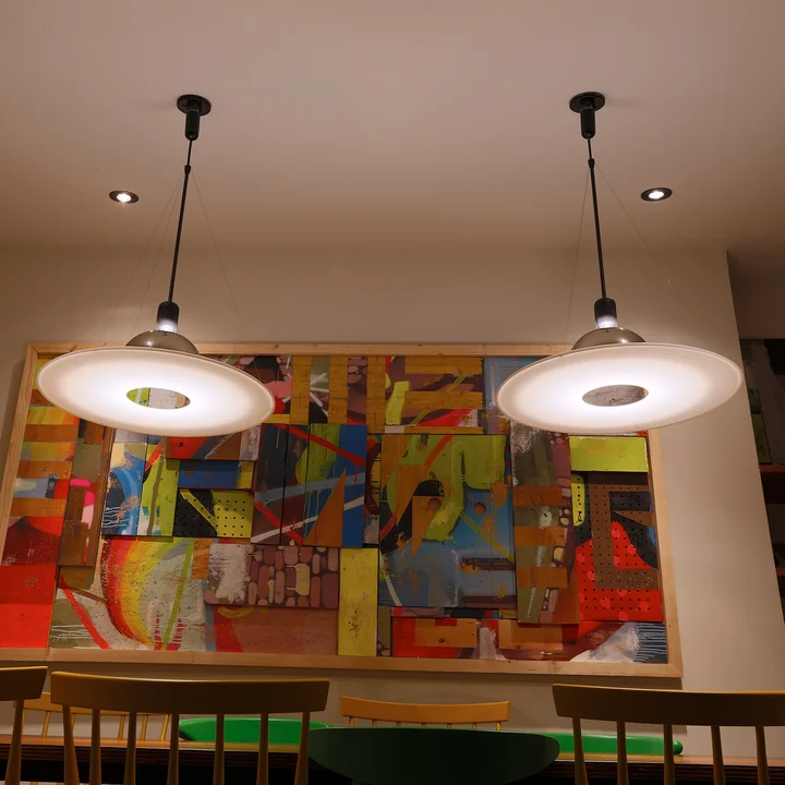 La lampe suspendue Frisbi de Flos au-dessus d'une table à manger devant une œuvre d'art colorée