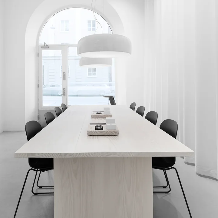 La lampe à suspension Smithfield Pro de Flos en blanc au-dessus d'une table en bois clair avec des chaises noires