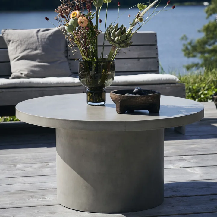 Stone La table d'appoint en béton de House Doctor devant un banc sur la terrasse